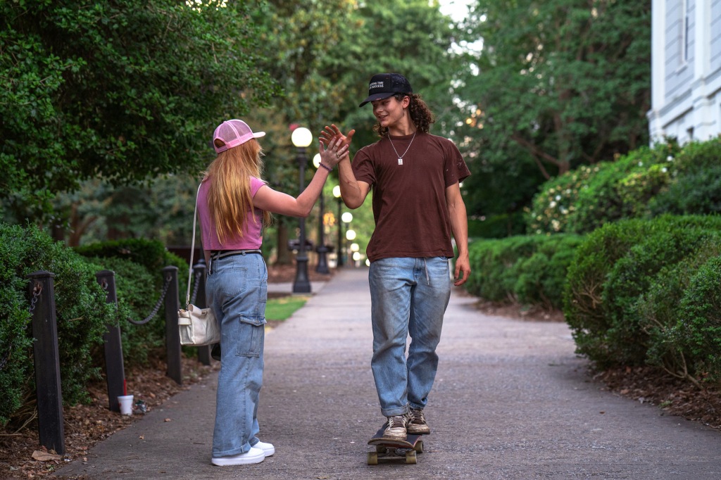 A guy skateboarding and high-fiving his friend.